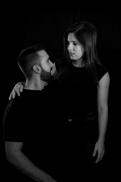 Portrait of a young couple in black and white with black\
background looking into each other39s eyes