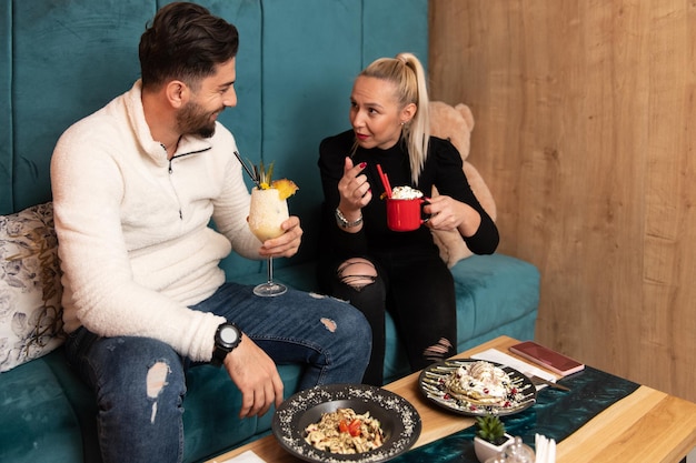 Portrait of Young Couple Eating Pancakes in Restaurant and Drinking Cocktail Chill and Colada