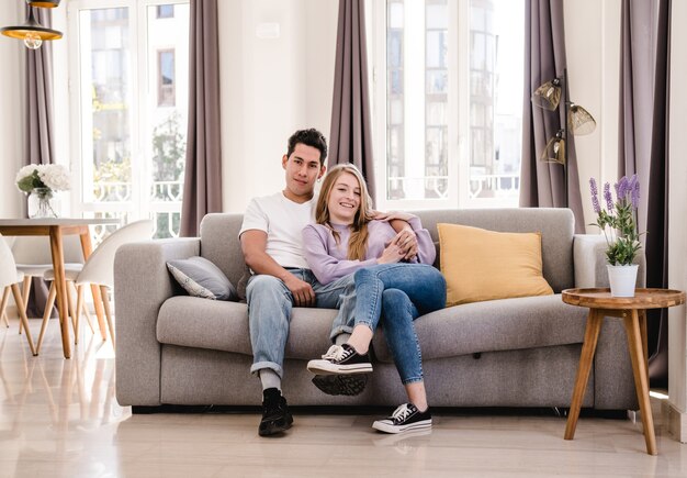 Ritratto di giovane coppia sorridente e godendo insieme seduti sul divano di casa.