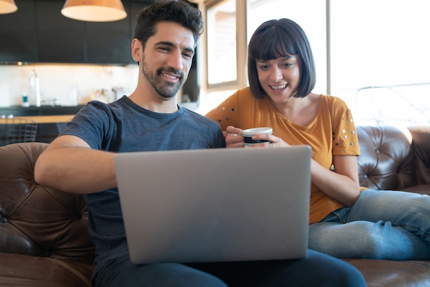 Portrait of young couple spending time together and using laptop while sitting on couch at home.