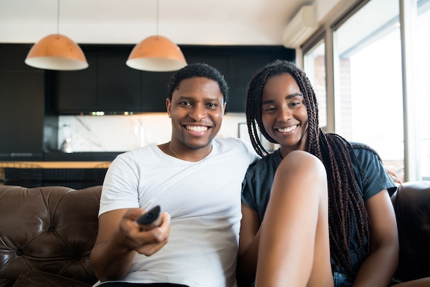 Portrait of young couple spending time together and watching tv series or movies while sitting on couch at home.