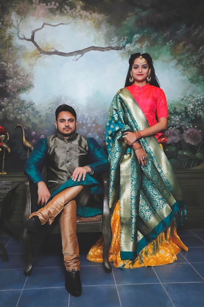 Portrait of young couple in traditional indian attire standing against a designed wall