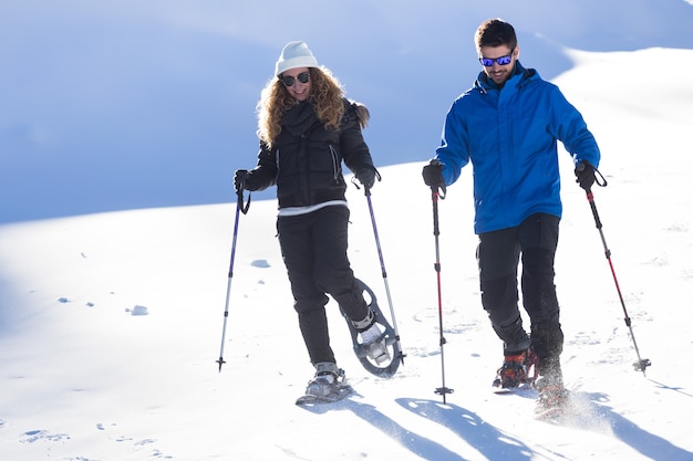 Ritratto di giovane coppia che cammina con le racchette da neve su sfondo invernale.