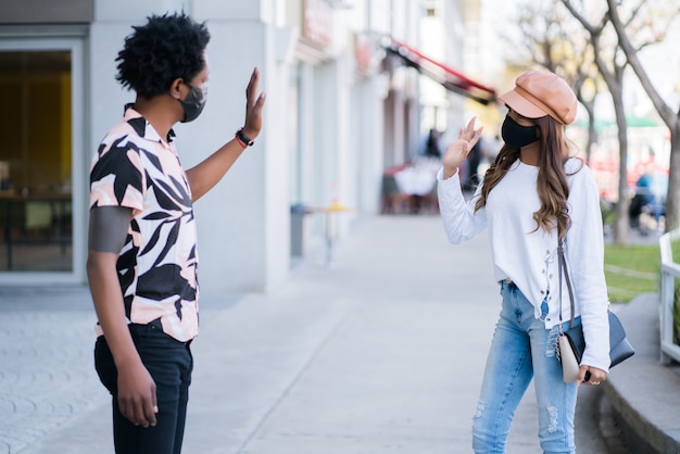 Portrait of young couple wearing protective mask and keeping distance while wave hand to greet each other