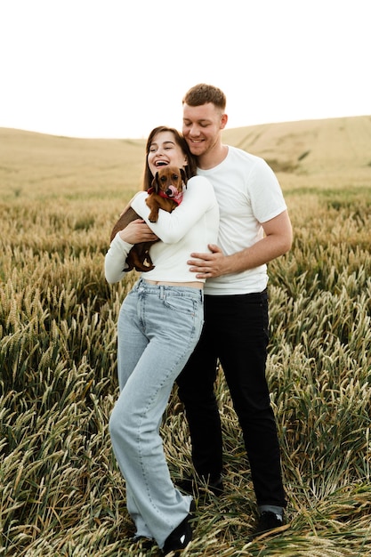 Portrait of a young couple with a pet. the guy hugs the girl holding the dog. people in love walking along the field with a dog.lovers with a dog