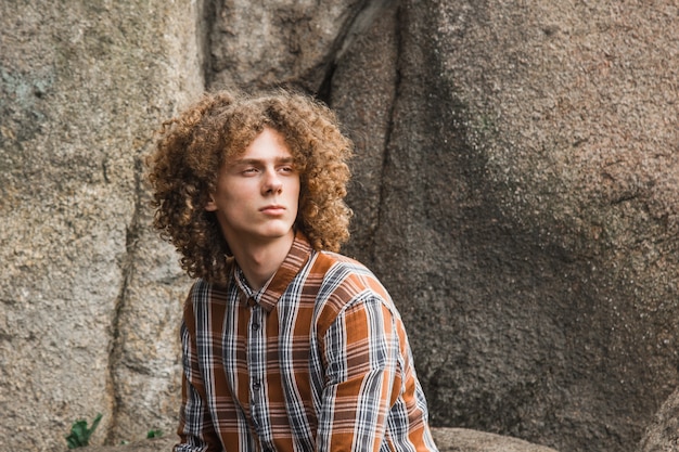 Portrait of a young curly haired guy among the stones 