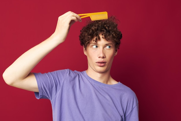 Portrait of a young curly man in purple tshirts with a comb isolated background