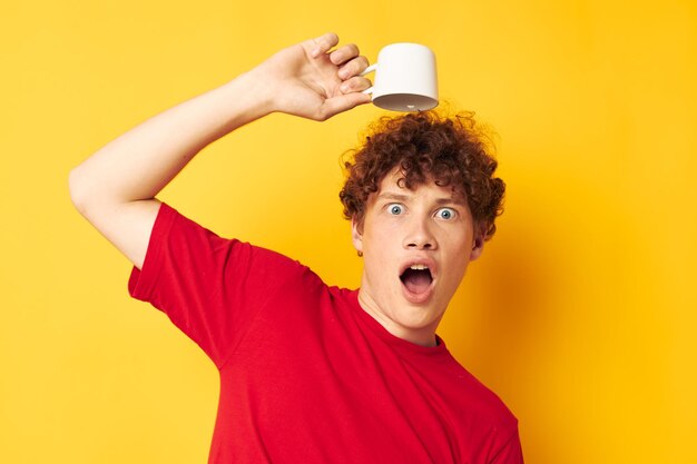 Portrait of a young curly man white mug in the hands of a drink yellow background unaltered