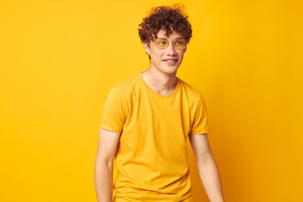 Portrait of a young curly man yellow tshirt glasses fashion hand gestures isolated background unaltered