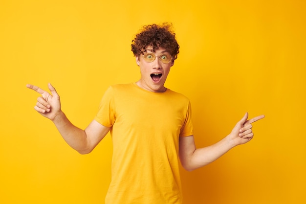 Portrait of a young curly man yellow tshirt glasses fashion hand gestures isolated background unaltered