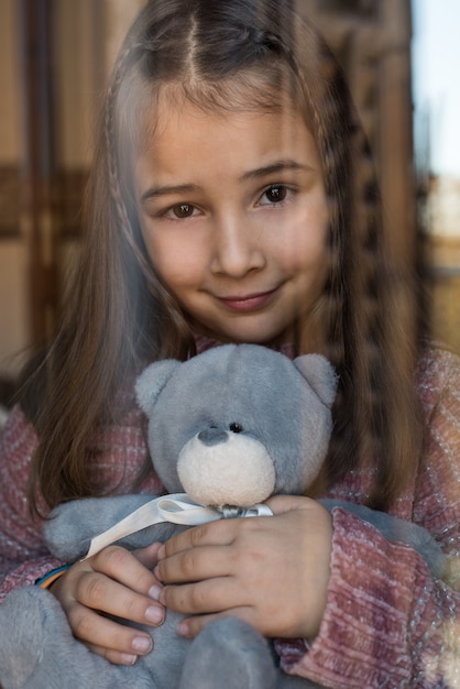 Ritratto di una giovane ragazza carina guardando attraverso la finestra con orsacchiotto