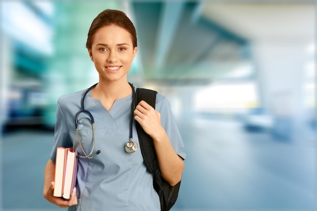 Portrait of young cute woman doctor with books on clinic background