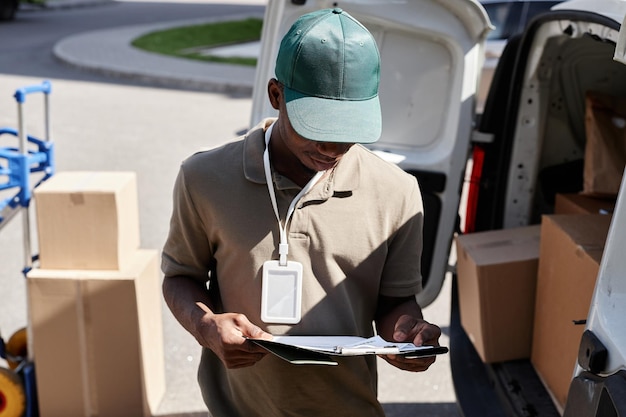 Portrait of young delivery man checking documents while\
unloading delivery van