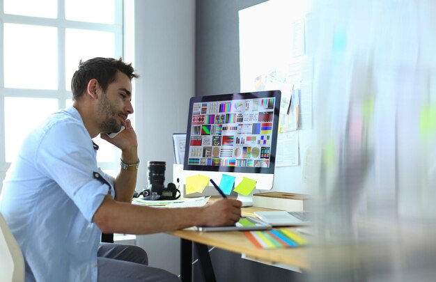 Portrait of young designer sitting at graphic studio in front of laptop and computer while working online