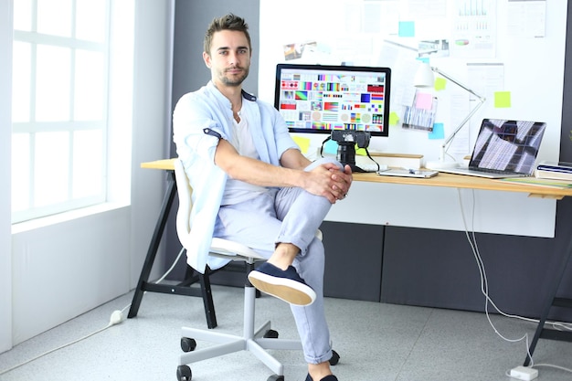 Portrait of young designer sitting at graphic studio in front of laptop and computer while working online