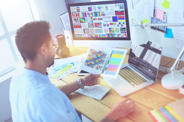 Portrait of young designer sitting at graphic studio in front of laptop and computer while working online