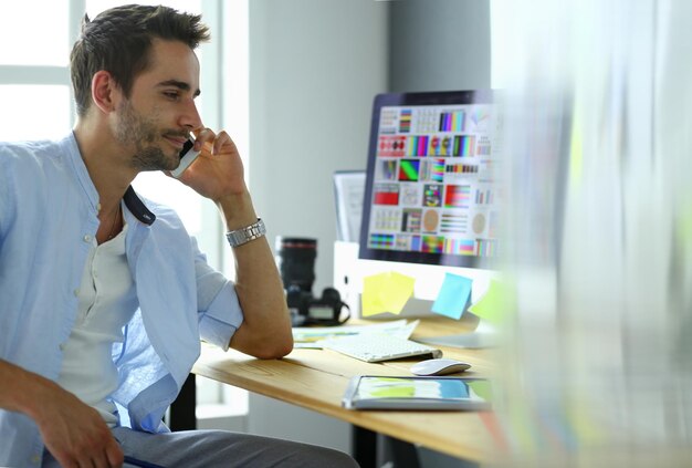 Portrait of young designer sitting at graphic studio in front of laptop and computer while working online