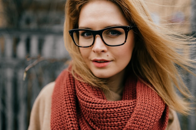 Ritratto di giovane ragazza bionda elegante con occhiali e sciarpa in posa all'aperto