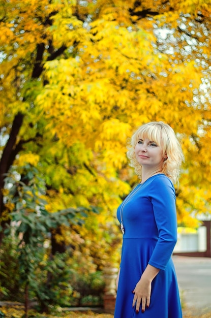 Portrait of young elegant blonde woman with blue eyes walking in streets of autumn city. Blue dress