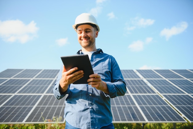 The portrait of a young engineer checks with tablet operation with sun cleanliness on field of photovoltaic solar panels Concept renewable energy technology electricity service green power