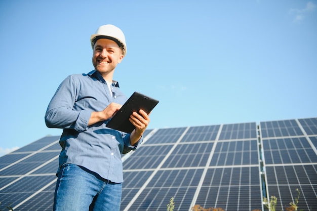 The portrait of a young engineer checks with tablet operation with sun cleanliness on field of photovoltaic solar panels Concept renewable energy technology electricity service green power