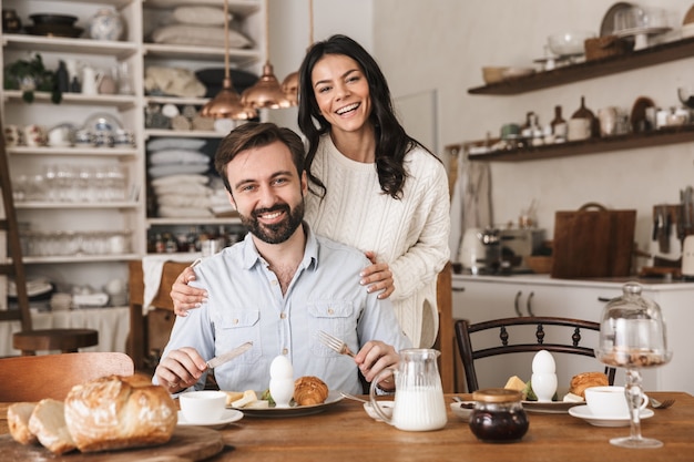 自宅のキッチンで朝食をしながらテーブルで食べる若いヨーロッパのカップルの男性と女性の肖像画