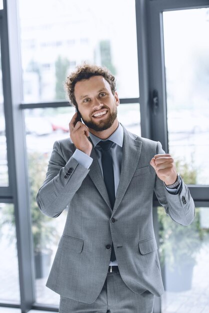 Portrait of young excited businessman talking on smartphone in office