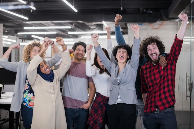 portrait of young excited multiethnics business team of software developers standing and looking at camera while celebrating success at modern startup office