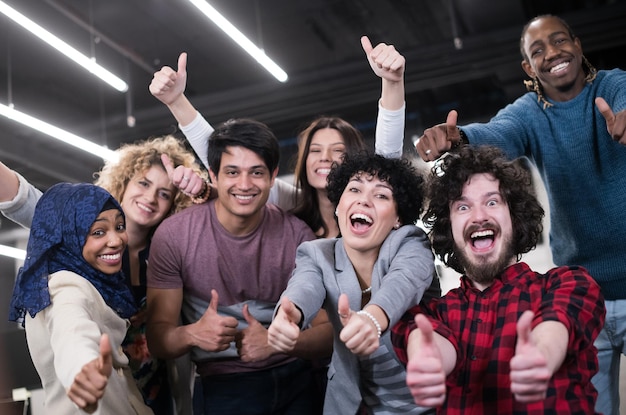 Ritratto di un giovane eccitato team aziendale multietnico di sviluppatori di software in piedi e guardando la fotocamera mentre celebra il successo nel moderno ufficio di avvio