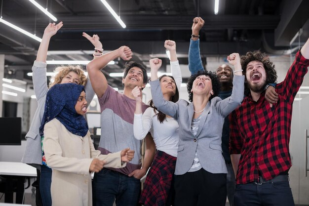 portrait of young excited multiethnics business team of software developers standing and looking at camera while celebrating success at modern startup office