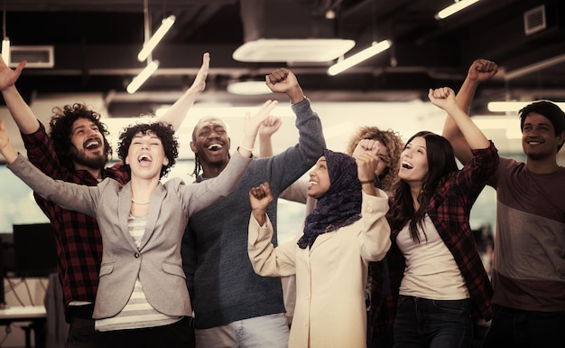 portrait of young excited multiethnics business team of software developers standing and looking at camera while celebrating success at modern startup office