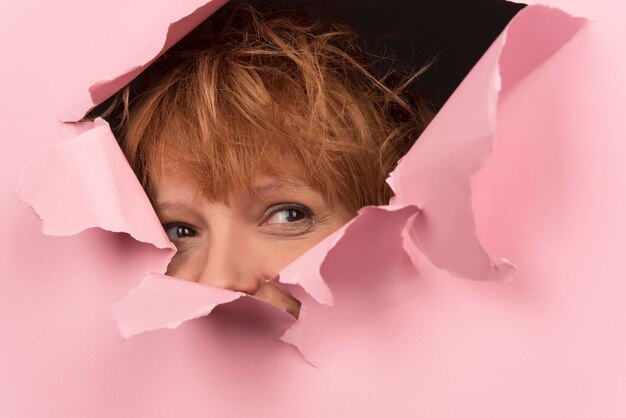 Portrait of young excited woman shocked by commercial offer,\
looking through hole in torn paper