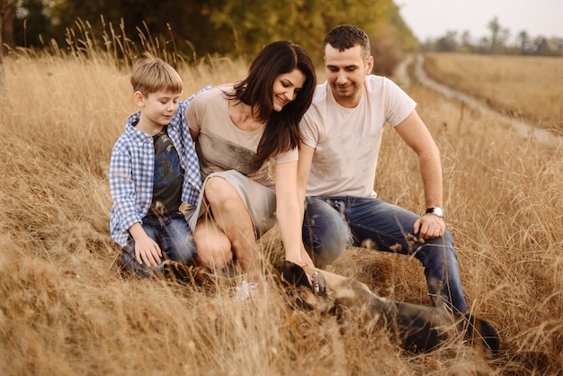 Portrait of a young family who plays with a dog on nature in the autumn afternoon