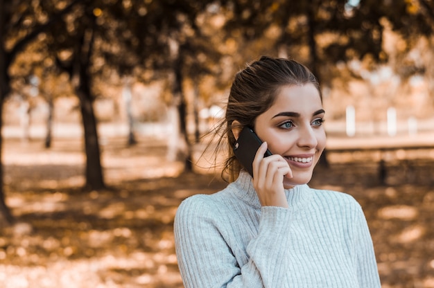 Portrait of young fascinating cute woman talking on mobile phone in park.