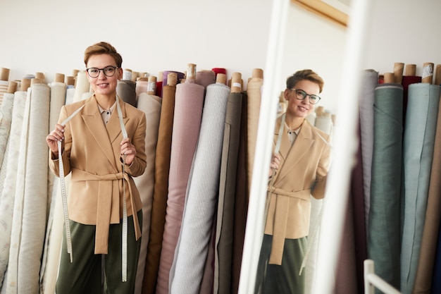 Portrait of young fashion designer in eyeglasses standing with tape measure