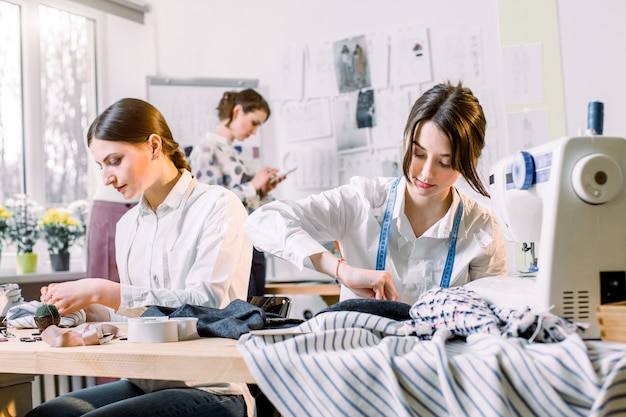 Photo portrait of young fashion dressmakers women at work. dressmaker, tailor, fashion and showroom concept - portrait of talented female dressmakers working with textile for sewing clothes