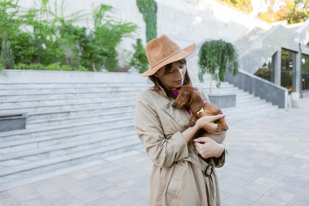 若いファッションの女性と都市公園の素敵なダックスフントの子犬の肖像画。愛人とペット