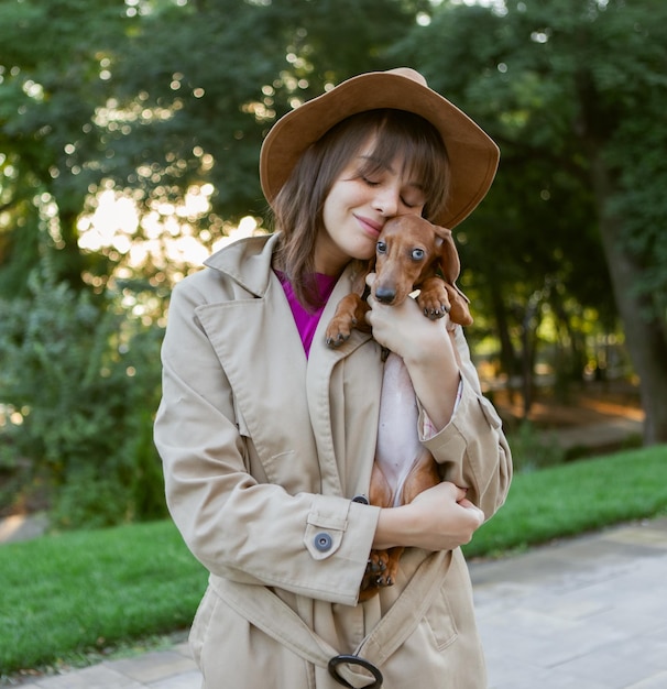 若いファッションの女性と都市公園の素敵なダックスフントの子犬の肖像画。愛人とペット