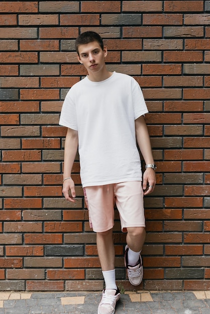 Photo portrait of young fashionably dressed man on the background of brick street wall lgbt community