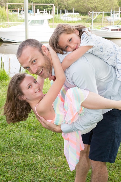 Портрет молодого отца с одной дочерью на спине и другой девочкой впереди на спине