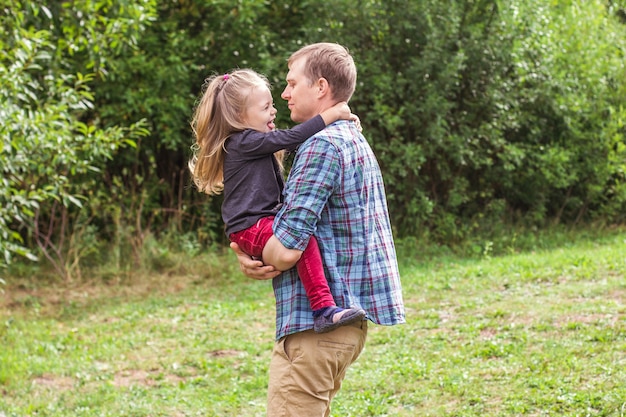 Portrait of a young father and daughter 2-3 years old looking at the camera and playing on the summer lawn in the park