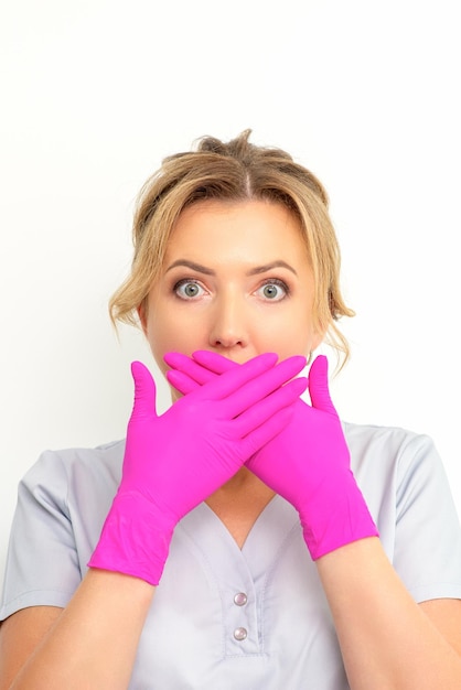 The portrait of a young female caucasian doctor or nurse is shocked covering her mouth