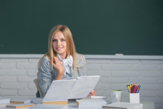 Portrait of young female college student reading book studying in classroom on class with blackboard...