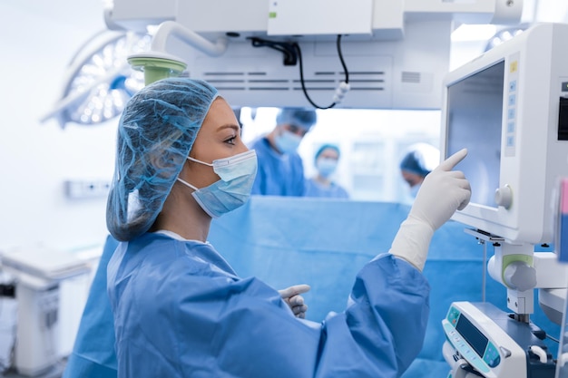 Portrait of a young female doctor in scrubs and a protective face mask preparing an anesthesia machine before an operation