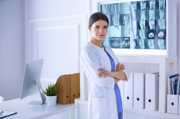 Портрет молодой женщины-врача в белом халате, стоящей в больнице со скрещенными руками