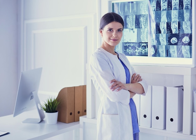 Portrait of young female doctor in white coat standing in hospital with her hands crossed