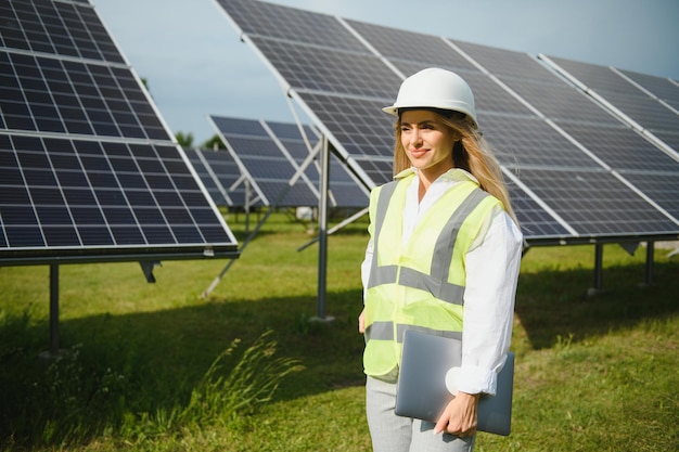 Portrait of young female engineer standing near solar panels Beautiful female professional in white helmet