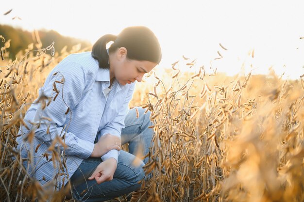 Portrait of young female farmer standing in soybean field examining crop