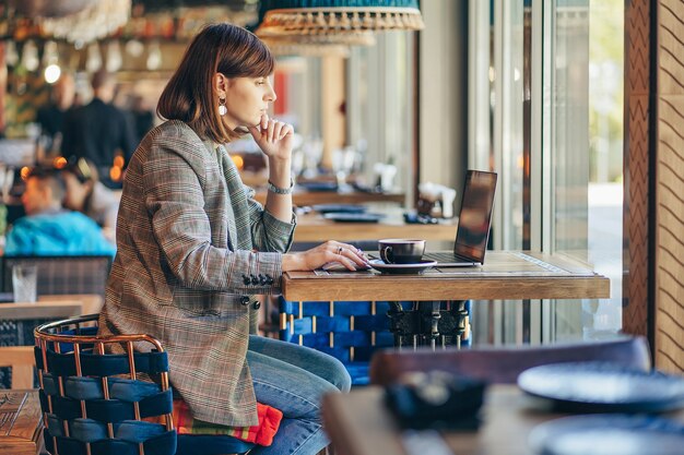 Photo portrait of a young female freelancer using laptop computer for distance job while sitting in cafe.