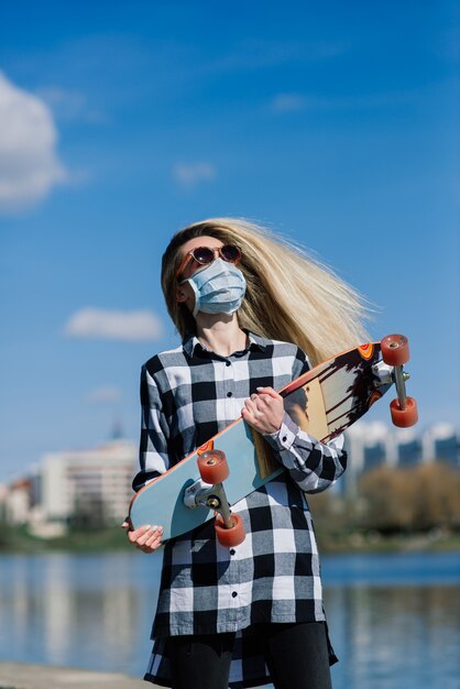 Portrait of a young female in a medical mask with longboard in the city during the quarantine